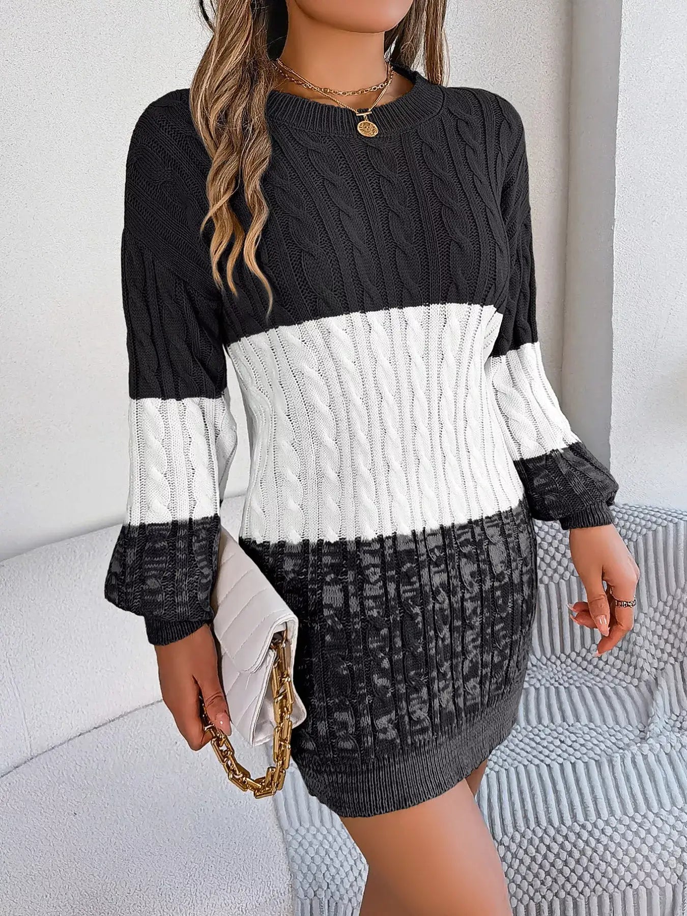 Woman wearing color block cable knit sweater dress with textured pattern, holding a clutch. Acrylic material, slightly stretchy.