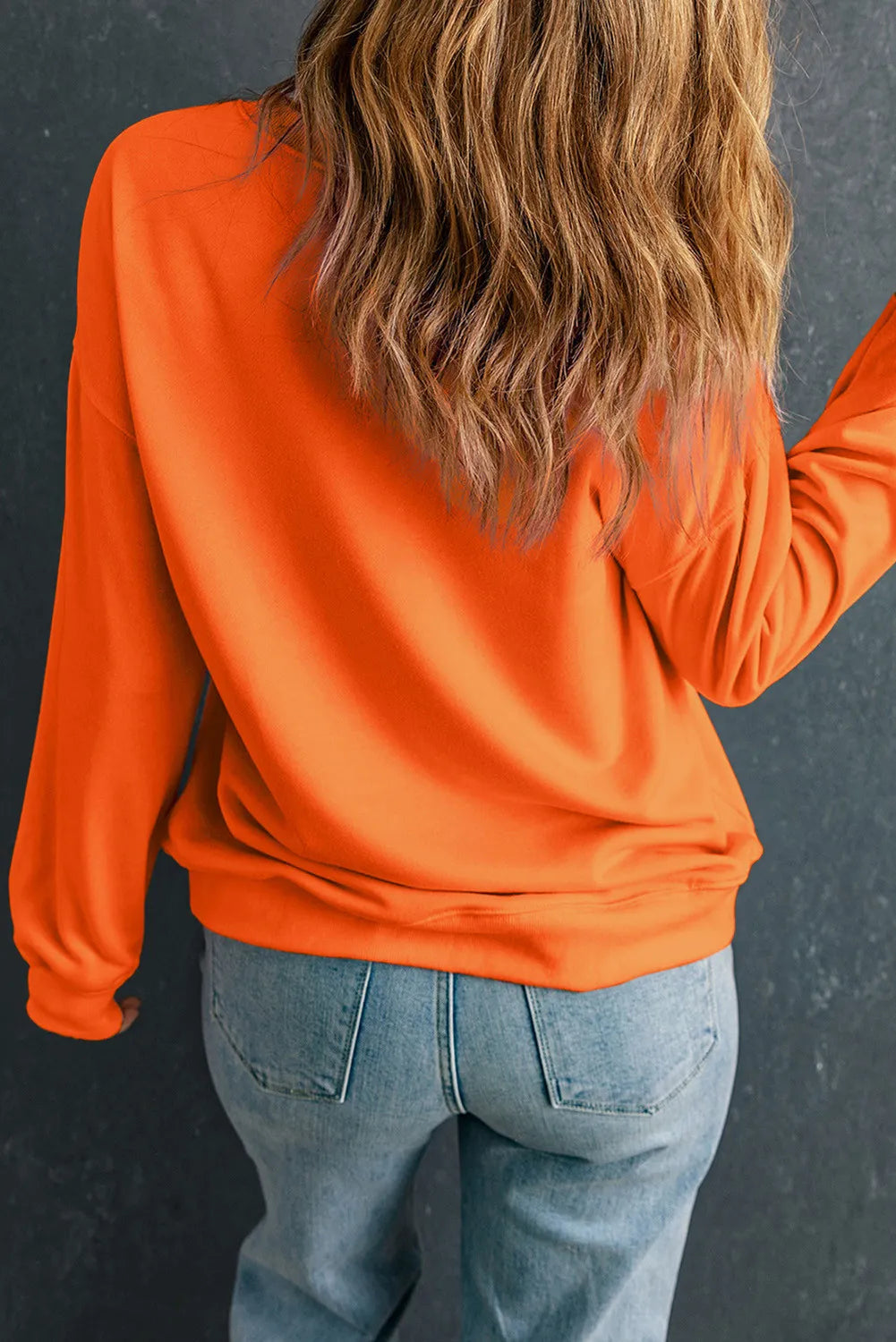 Person wearing orange Game Day Sweatshirt with long sleeves and round neck, paired with jeans.