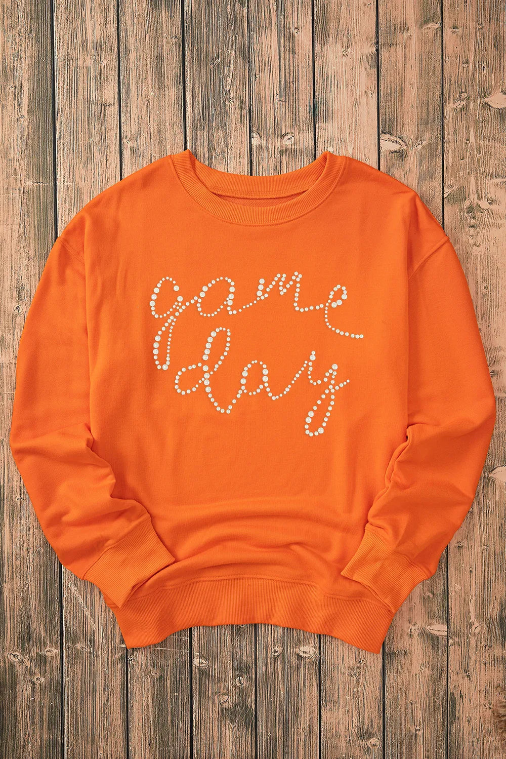 Orange Game Day Sweatshirt with round neck and long sleeves on wooden background