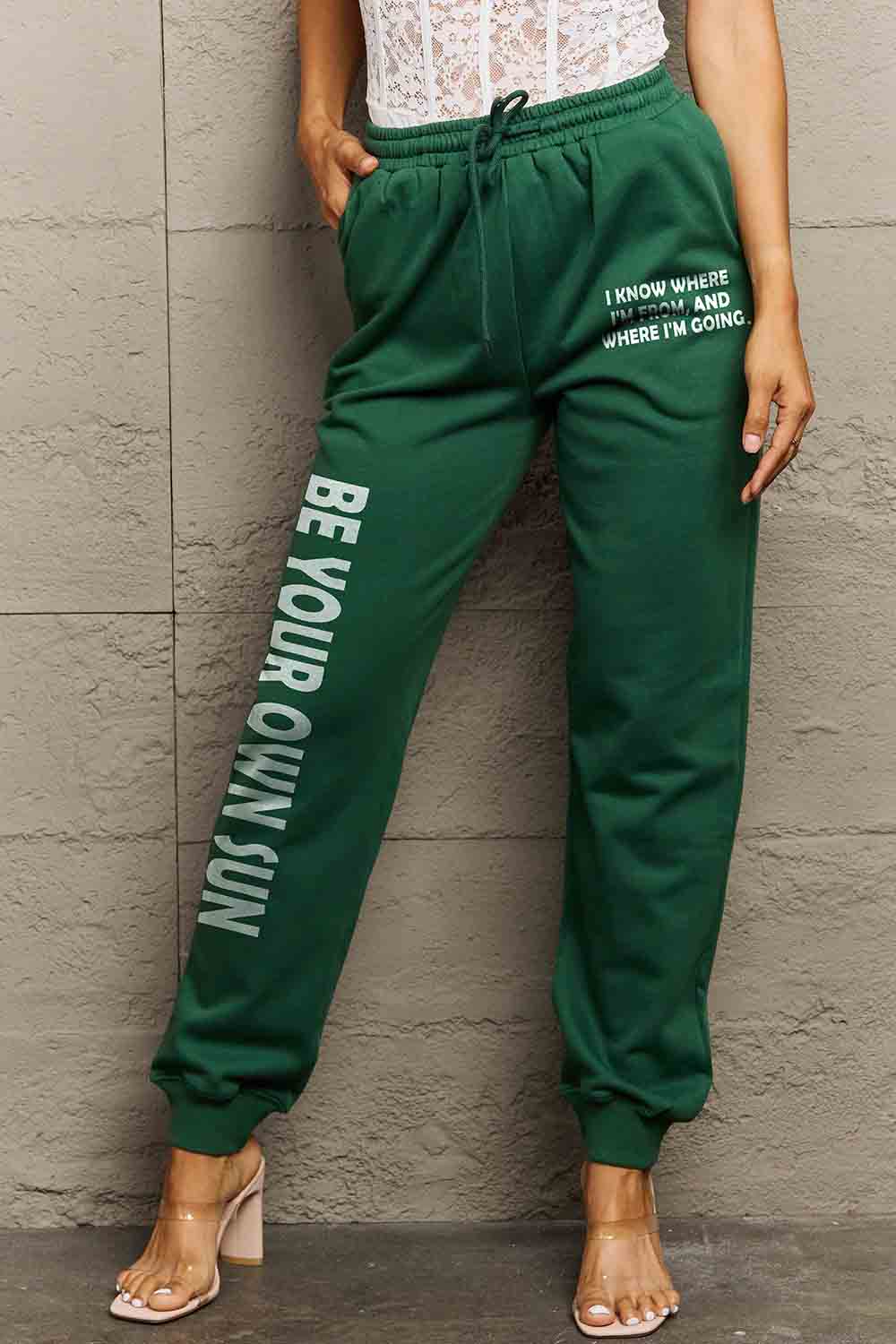 Person wearing Graphic Sweatpants with 'BE YOUR OWN SUN' print, featuring adjustable drawstring waistband, cozy fit, and motivational design.