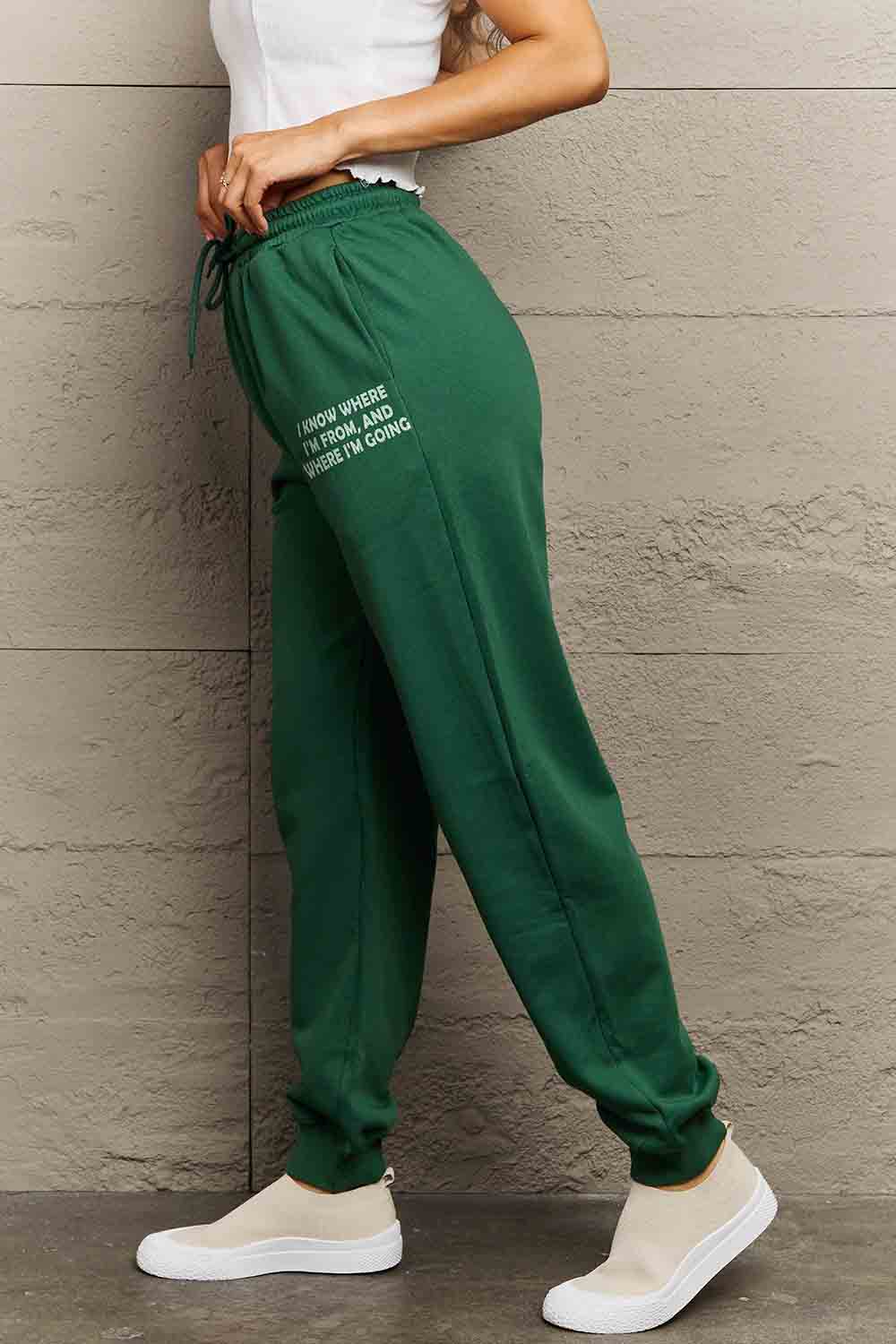 Woman wearing green Graphic Sweatpants with 'BE YOUR OWN SUN' print, showcasing relaxed fit and drawstring waistband.