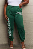 Woman wearing Graphic Sweatpants with 'BE YOUR OWN SUN' print, green color, drawstring waistband, full-size design.