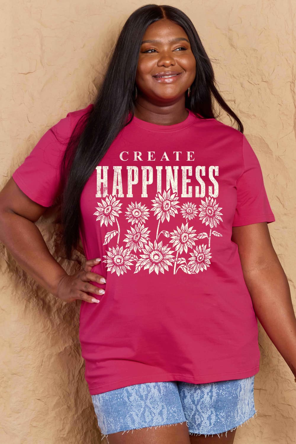 Woman wearing Graphic Cotton T-Shirt with CREATE HAPPINESS print standing against a beige background.