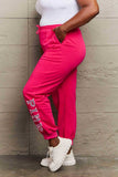 Side view of woman wearing Graphic Sweatpants with PINK print, featuring drawstring waistband, ideal for workouts or casual wear.