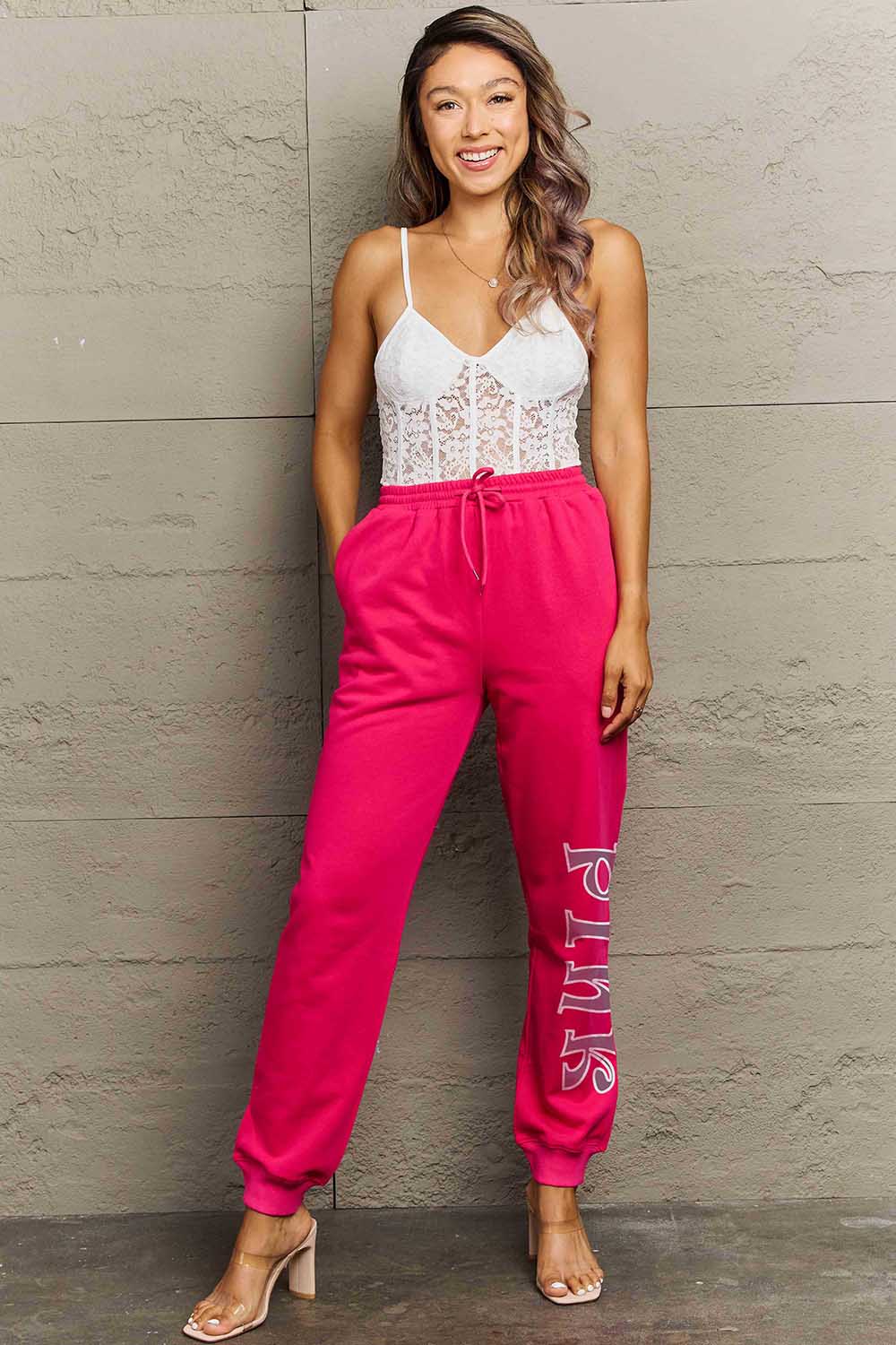 Woman wearing Graphic Sweatpants with bold PINK print and drawstring waistband, showcasing style and comfort.