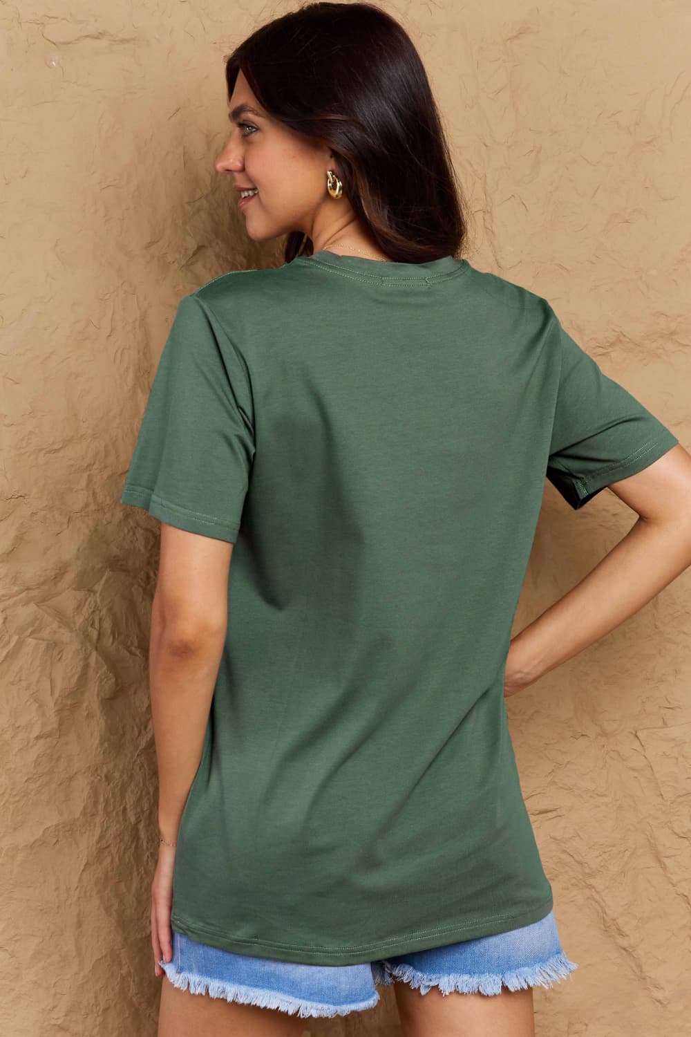 Rear view of woman wearing Graphic Cotton T-Shirt in green, paired with denim shorts, showcasing casual style with 'TEACHER VIBES' motif.