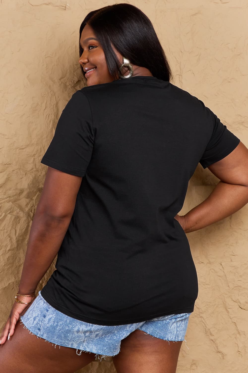 Back view of a black Graphic Cotton T-Shirt with "TEACHER VIBES" print, worn by a model in denim shorts.