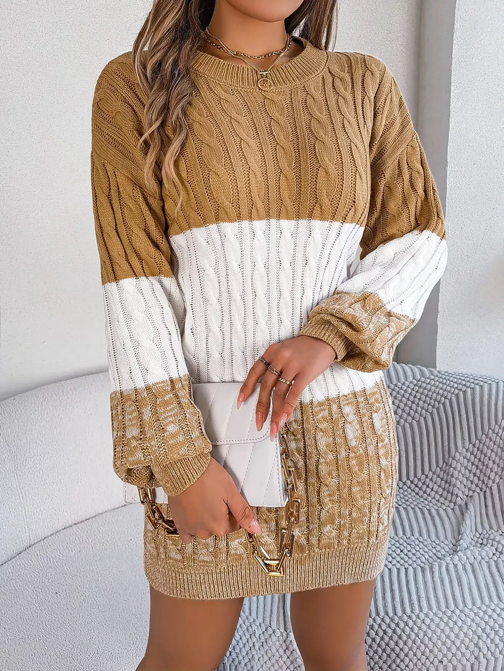 Woman wearing a color block cable knit sweater dress with textured pattern, brown and white tones, slightly stretchy, 100% acrylic material.